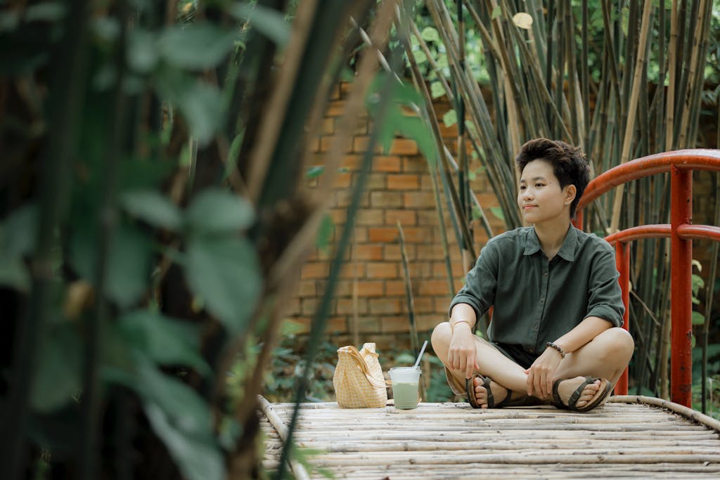 A person enjoys a serene moment on a bamboo bridge, surrounded by greenery outdoors.