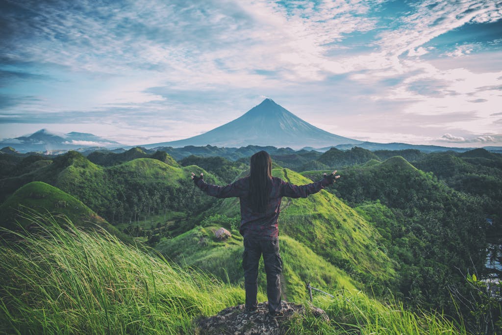 A person enjoys an expansive view of Mt. Mayon amidst lush green hills in Bicol, Philippines.