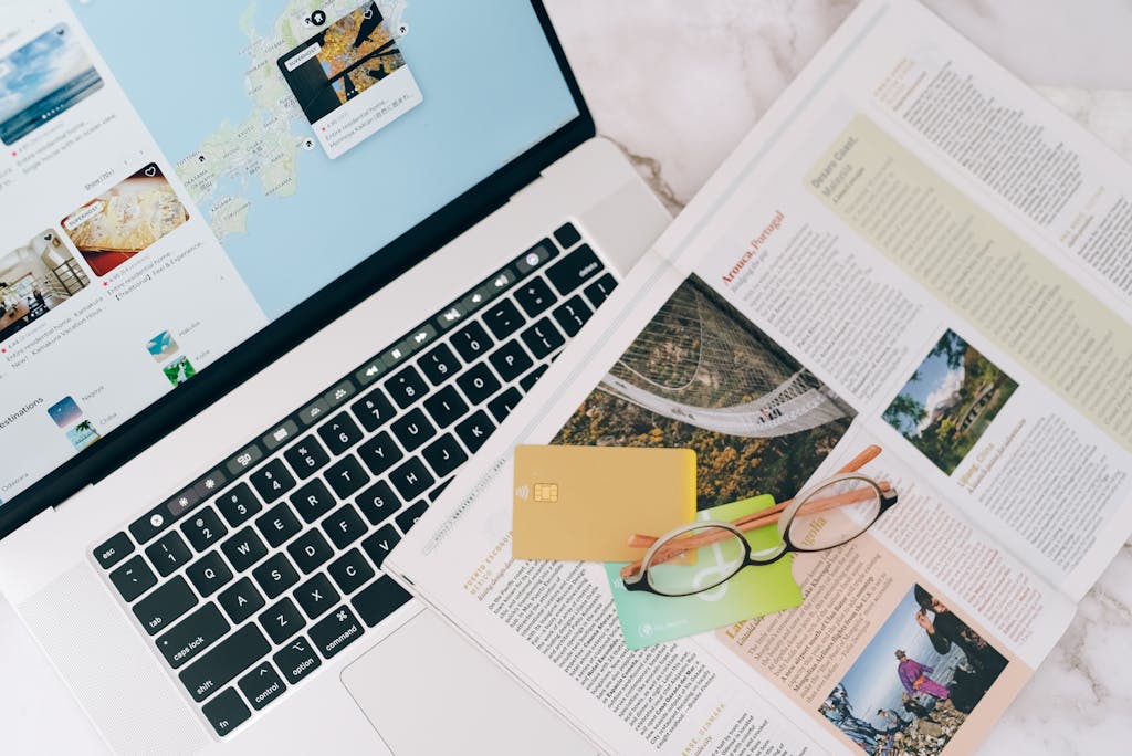 A top view of travel planning essentials on a laptop with a map, credit cards, and a magazine.