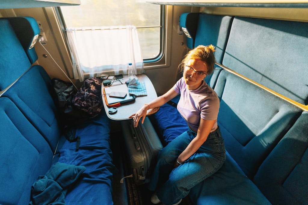 Woman sitting comfortably in a train compartment with blue seats, enjoying the journey.