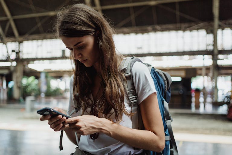 A young woman checks her smartphone while traveling at a train station.