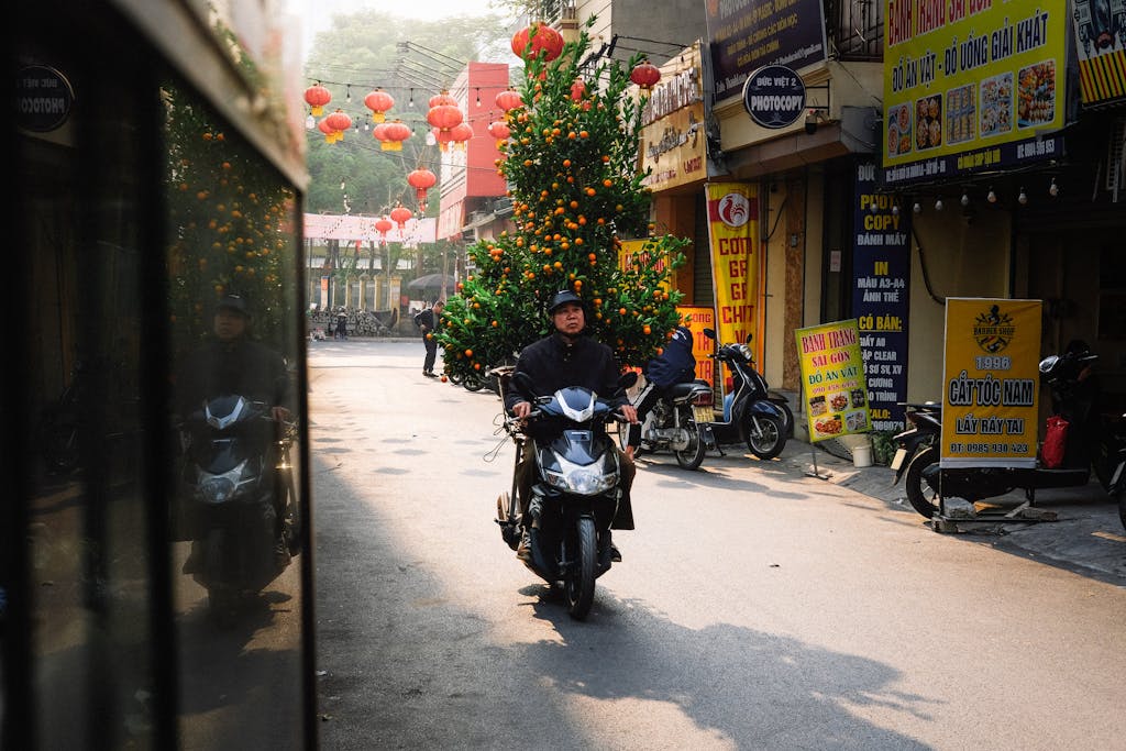 A motorcyclist rides through a Vietnamese street adorned with red lanterns and greenery.