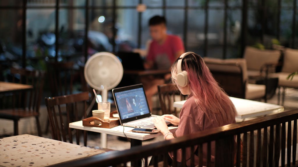 A woman with headphones edits a video on her laptop in a cozy café environment, Vietnam.